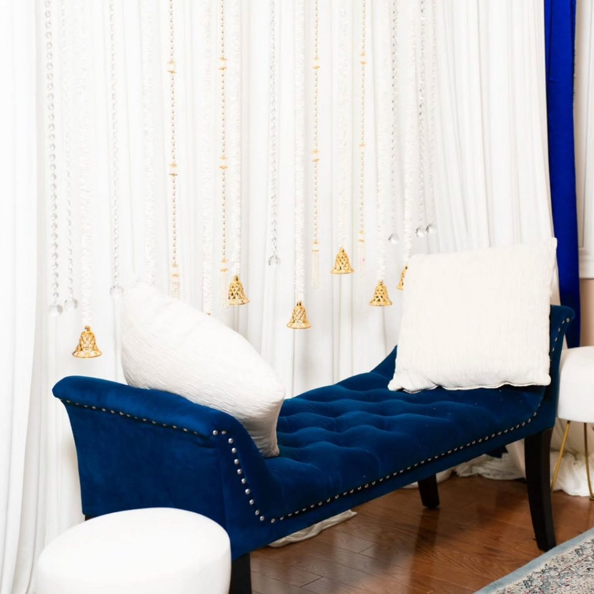 Close-up of a royal-blue tufted bench with white cushions beneath hanging crystal strands and gold bells